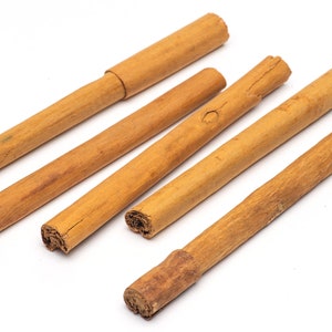 May include: Five cinnamon sticks of varying lengths, arranged in a fan shape on a white background.