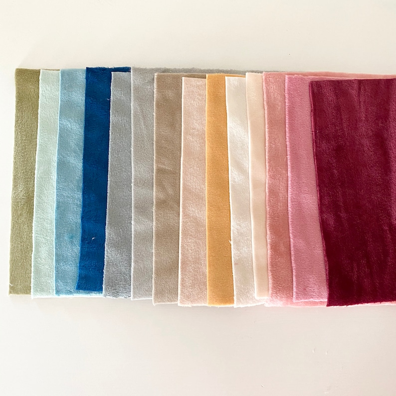 May include: A collection of rectangular fabric swatches arranged in a row, featuring a variety of colors including olive green, light blue, navy, gray, beige, cream, yellow, white, pale pink, dusty rose, and a deep burgundy red velvet texture.
