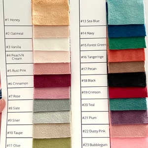 May include: A color swatch chart for Smooth Minky Fabric 100% Polyester by rovi. The chart displays 24 numbered fabric samples in various colors including honey, oatmeal, vanilla, peach, rust, cinnamon, rose, slate, silver, taupe, olive, mint, sea blue, navy, forest green, tangerine, pecan, black, crimson, teal, plum, dusty pink, bubblegum, and electric red.