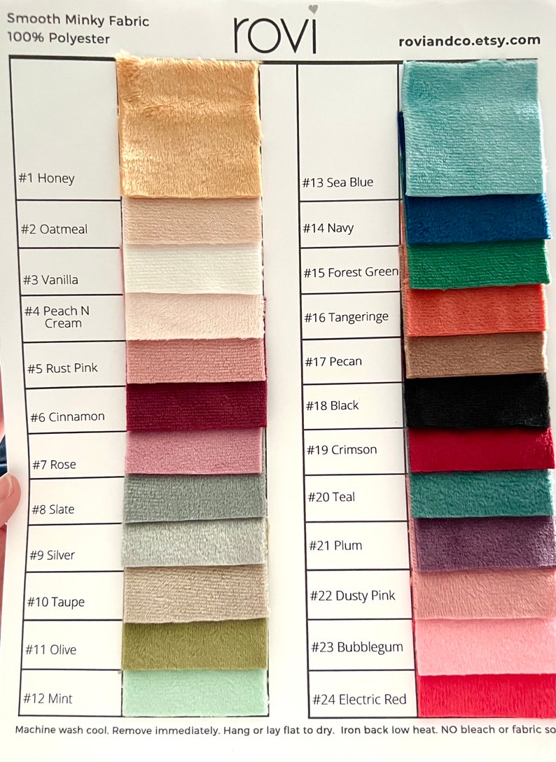 May include: A color swatch chart for Smooth Minky Fabric 100% Polyester by rovi. The chart displays 24 numbered fabric samples in various colors including honey, oatmeal, vanilla, peach, rust, cinnamon, rose, slate, silver, taupe, olive, mint, sea blue, navy, forest green, tangerine, pecan, black, crimson, teal, plum, dusty pink, bubblegum, and electric red.