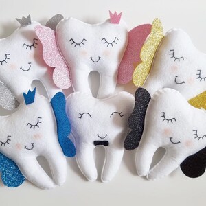 May include: A set of ten plush tooth-shaped toys with different colored glitter accents. Each tooth has a different facial expression and a crown on top.