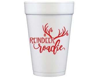 Puede incluir: Un vaso de espuma blanco con un gráfico rojo de astas de reno adornadas con pequeños adornos colgantes. Debajo de las astas, el texto REINDEER en fuente de bloque y roadie en letra cursiva está centrado en la parte frontal del vaso.