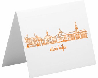 May include: Orange line drawing of a city skyline with the text "olivia keifer" below.