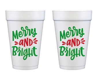 Puede incluir: Dos vasos de espuma blancos con el texto Merry and Bright impreso en tinta verde y roja. La frase Merry and Bright está escrita en una fuente cursiva estilizada, con la palabra AND en letras mayúsculas rojas entre las líneas de texto.