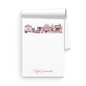 Puede incluir: Un bloc de notas blanco con un dibujo a tinta roja de un horizonte de ciudad y el texto "Peyton Drummond" en la parte inferior.