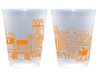 May include: Two clear plastic cups with a city skyline design in orange. The design includes buildings, a clock tower, and a taxi cab. The cups are translucent and have a slightly frosted appearance.