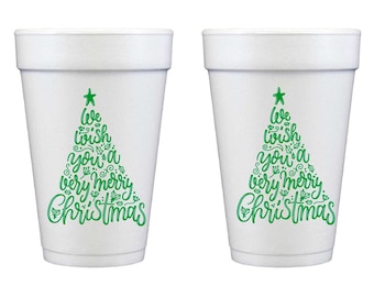 Puede incluir: Dos vasos de poliestireno blanco con un diseño gráfico verde en forma de árbol de Navidad. El texto dentro del árbol dice We wish you a very merry Christmas, acentuado con pequeñas hojas de acebo y ramitas, coronado con una estrella verde.