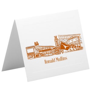 Puede incluir: Una tarjeta blanca con una ilustración naranja del campus de la Universidad de Texas en Austin, que incluye la icónica torre, el estadio y un letrero que dice "Texas". La tarjeta también incluye el texto "Ronald Mullins".