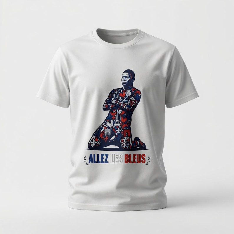 May include: White t-shirt featuring a graphic of a soccer player kneeling with arms crossed. The player's uniform is patterned with red, white, and blue designs. The text "ALLEZ LES BLEUS" is printed below the image.