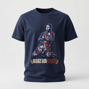 May include: Navy blue t-shirt featuring a graphic of a soccer player kneeling with arms crossed. The player's uniform is decorated with red, white, and blue patterns. The text "ALLEZ LES BLEUS" is printed below the player.