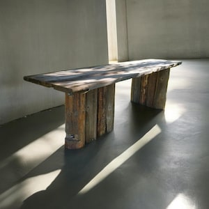 Puede incluir: Una mesa de madera rústica con una tapa larga y rectangular y cuatro patas hechas de tablones de madera apilados. La mesa está hecha de madera recuperada y tiene un acabado natural y desgastado.