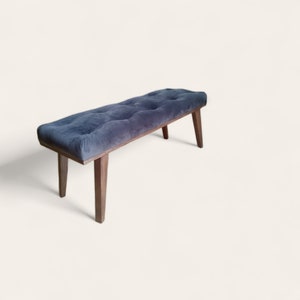 Puede incluir: Un banco tapizado de color gris oscuro con la parte superior capitoné y cuatro patas de madera.