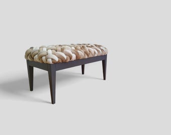 May include: A rectangular upholstered bench with a woven top in shades of beige and brown. The bench has a dark brown wooden frame and four tapered legs. The design is modern and the neutral colors would complement various interior styles.