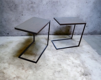 May include: Two gray concrete side tables with black metal frames. The tables are on a gray concrete floor.