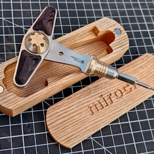 Könnte beinhalten: Ein Präzisionswerkzeug mit einem Gehäuse aus Edelstahl und Messing, mit einem Holzgriff und einer passenden Holzkiste. Die Kiste ist mit dem Wort "miroc" graviert. Das Werkzeug ist für Detailarbeiten konzipiert.