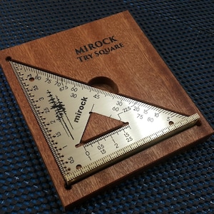 Könnte beinhalten: Ein Messing-Winkelmesser mit einer Holzbasis. Der Winkelmesser ist in Grad und Zoll unterteilt. Die Basis ist mit "MIROCK TRY SQUARE" beschriftet.