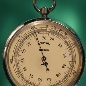 May include: A silver pocket-sized barometer with a white face and black markings. The face reads "COMPENS. N№63635" and has a scale from 500 to 3000. The needle points to 76.