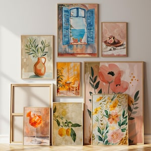 May include: A collection of framed art prints featuring watercolor paintings. The artwork includes a vase with olive branches, a window overlooking the sea, a still life of figs, and floral and citrus themes. The frames are a light wood color.