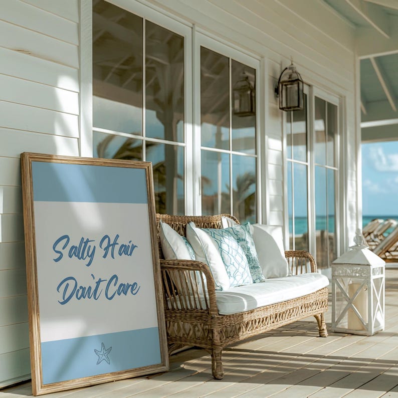 May include: A wooden framed sign with a blue background and white text that reads "Salty Hair Don't Care". A starfish is in the bottom right corner of the sign. The sign is leaning against a wicker couch with white cushions on a porch.