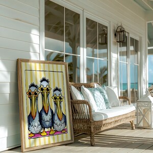 May include: A framed print of three cartoon pelicans wearing sunglasses on a yellow and white striped background. The print is leaning against a wicker sofa on a porch.