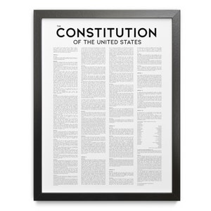 May include: A framed print of the United States Constitution. The black frame surrounds a white background filled with text. The title "THE CONSTITUTION OF THE UNITED STATES" is printed in bold black letters at the top.
