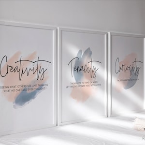 Könnte beinhalten: Drei gerahmte Drucke mit Aquarell-Hintergründen in Blautönen und Rosa. Die Drucke zeigen die Wörter "Kreativität", "Beharrlichkeit" und "Neugier" mit Definitionen unter jedem Wort.