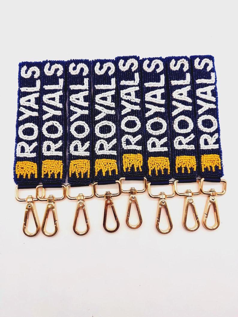 A collection of blue beaded straps with the word "ROYALS" in white beads. Each strap has a gold-colored clasp and a yellow beaded crow  at the bottom. The straps are displayed against a white background.