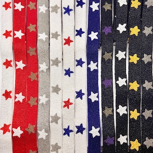 May include: A collection of narrow, vertical fabric straps decorated with repeating star patterns in various colors. The straps feature beaded textures in white, red, grey, blue, black, and yellow, arranged in parallel rows against contrasting backgrounds.