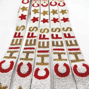 May include: White beaded straps with the word "CHIEFS" in gold and red. Each strap features a red horseshoe and star accents. The straps are likely for a sports-themed accessory.