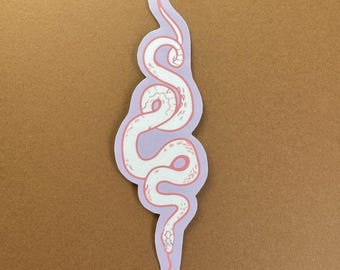 May include: A white snake sticker with a pink outline and details, set against a light purple background. The sticker has a unique, stylized design, perfect for decorating laptops, water bottles, or notebooks. The sticker is approximately 6 inches in length.