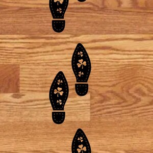 May include: Five black footprints with shamrock designs on a wood floor.