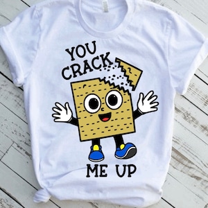 May include: White t-shirt with a cartoon image of a matzah cracker with a smiling face and the text "You Crack Me Up".