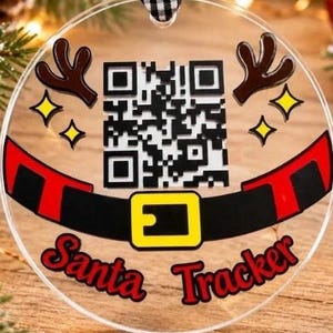 Könnte beinhalten: Ein runder, transparenter Acryl-Weihnachtsbaumschmuck mit einem schwarz-weißen QR-Code, braunem Rentiergeweih, gelben Sternen und einem schwarzen Weihnachtsmann-Gürtel mit gelber Schnalle. Der Text Santa Tracker steht in Rot darunter.