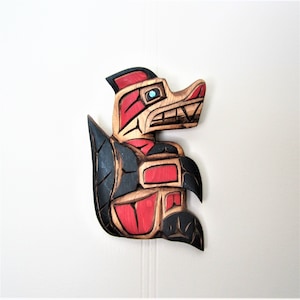 May include: A carved wooden sculpture of a red and black creature with a large mouth and sharp teeth. The sculpture is painted in red, black, and blue.