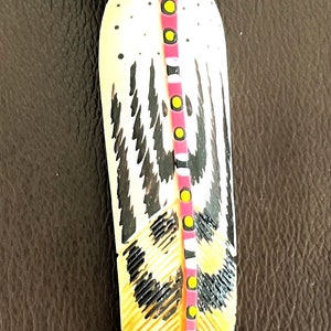 May include: A white, black, and pink feather with yellow and black dots. The feather is painted with a geometric design.