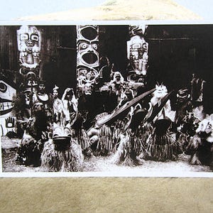 May include: Black and white photograph of a group of people in traditional attire, possibly a ceremonial gathering. The image features totem poles and individuals wearing masks and costumes, suggesting a cultural or historical theme.