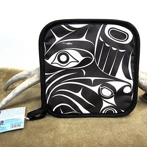 Könnte beinhalten: Schwarz-weißer Topflappen mit einem stilisierten Design eines Wals und anderer Meeresbewohner. Der Topflappen hat einen schwarzen Rand und einen schwarz-weißen Stoff mit einem Design eines Wals und anderer Meeresbewohner. Der Topflappen ist aus Stoff gefertigt und soll die Hände vor Hitze schützen.