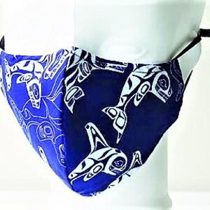 May include: Blue face mask with a white design of stylized orca whales. The mask has adjustable ear loops.
