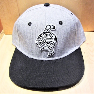 May include: A grey and black baseball cap with a black and white embroidered design of a stylised orca on the front.