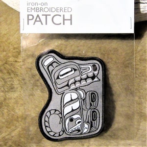 May include: Iron-on embroidered patch with a Native American design in grey, black, and white. The patch is in a clear plastic package with the words "iron-on EMBROIDERED PATCH" printed on a white label.