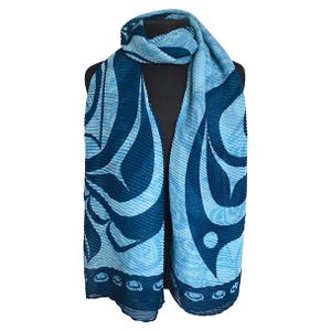 May include: A blue pleated scarf with a repeating pattern of stylized shapes. The scarf is displayed on a black mannequin. The scarf's design incorporates various shades of blue, and the edges have a decorative border.