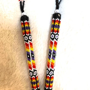 May include: Two beaded pen covers with a geometric pattern in black, white, orange, yellow, and purple. The beads are sewn together to create a colorful and intricate design.