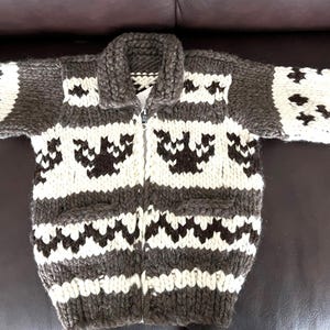 May include: A brown and white knitted cardigan with a zipper closure and a geometric pattern. The cardigan has a small pocket on each side.