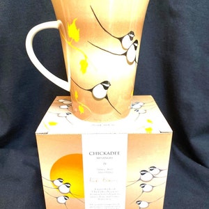 以下が含まれることがあります： 白い取っ手が付いた茶色のセラミックマグカップには、黄色の葉のついた枝に黒と白の鳥が描かれたデザインが施されています。マグカップは、同様のデザインと「CHICKADEE by MISANGIS」と「Birds & Branches」の文字が書かれた箱に入っています。