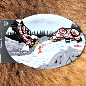 May include: A round, oval-shaped painting depicting a black bear and a white eagle with red, black, and white geometric patterns. The bear is in the foreground, facing left, and the eagle is in the background, facing right. Both animals are in a river with a waterfall and rocks. The painting is by Richard Shorty, Northern Tutchone.