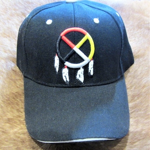 Può includere: Cappellino da baseball nero con visiera bianca e un simbolo di pace nativo americano ricamato con piume.