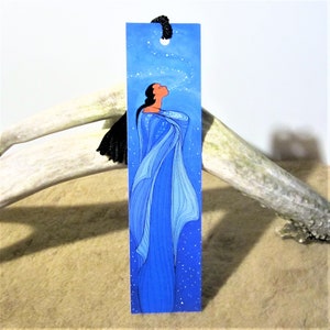 May include: A blue bookmark featuring a woman in a blue dress blowing on a stream of white stars. The background is a blue sky with white stars.