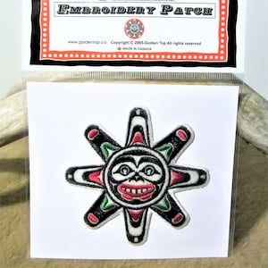 Peut inclure: Patch brodé représentant un soleil stylisé avec un visage en noir, blanc, rouge et vert. Le patch est sur un fond blanc.