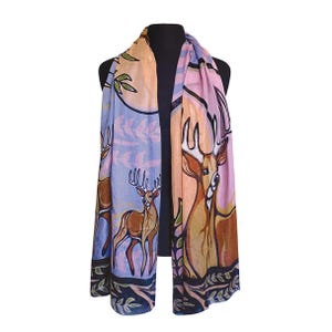 May include: A patterned scarf with a deer motif. The scarf displays a deer design against a backdrop of light blue, pink, and orange hues. The edges are trimmed with a dark blue border adorned with green foliage.