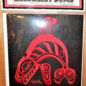 Può includere: Toppa ricamata rossa con una balena orca stilizzata su uno sfondo nero. La toppa è realizzata in Canada e presenta il testo "Embroidery Patch" e "Made in Canada".